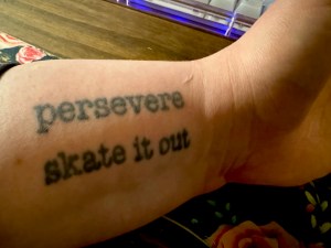 My left forearm and its two tattoos, one on top of the next, reading “persevere” and “skate it out” in typewriter-style lettering